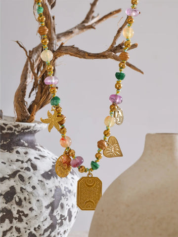 Colorful beaded necklace with starfish and heart charms hanging over a textured vase.