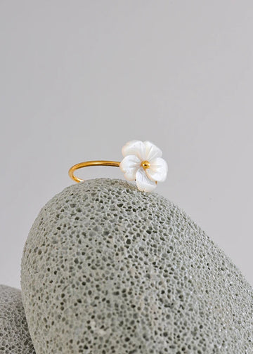 Gold earring with a white flower on a textured gray surface