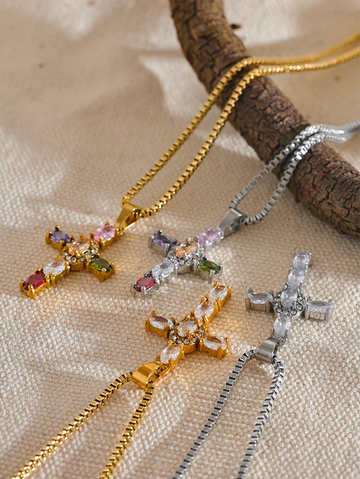 four golden and silver cross-shaped necklaces with gemstones on a textured surface