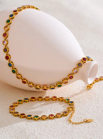 Gold bracelet and necklace with colorful gemstones on a white surface