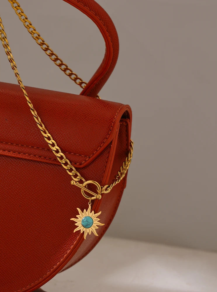 Red handbag with a gold chain and sun-shaped pendant on a neutral background