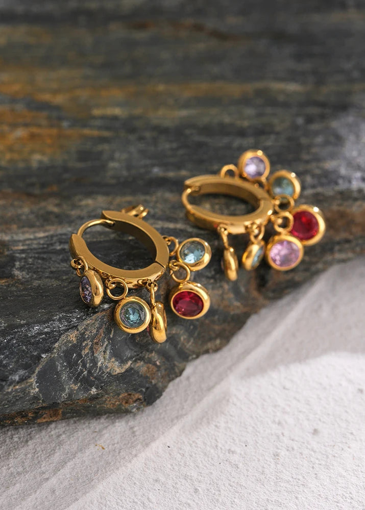 Gold earrings with colorful gemstones on a stone surface