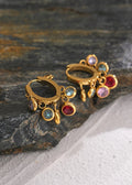 Gold earrings with colorful gemstones on a stone surface