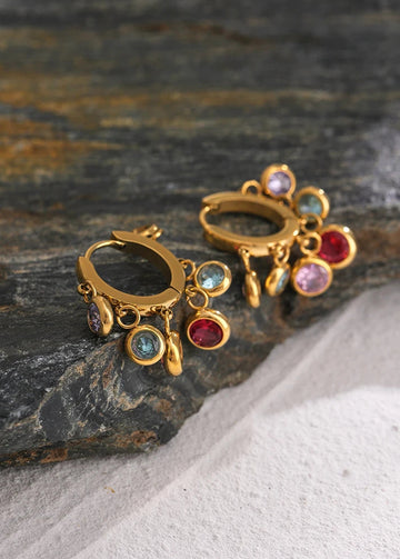Gold earrings with colorful gemstones on a stone surface