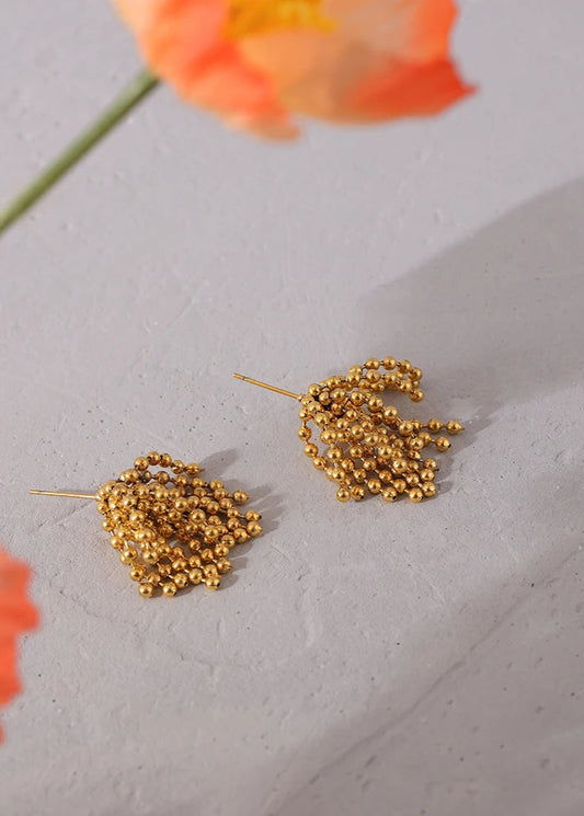 Gold leaf-shaped earrings on a light gray surface with an orange flower in the background.