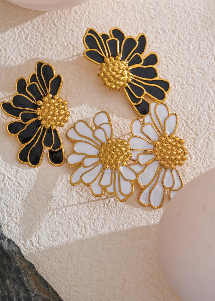 Pair of floral earrings with black, gold, and white colors on a textured surface.