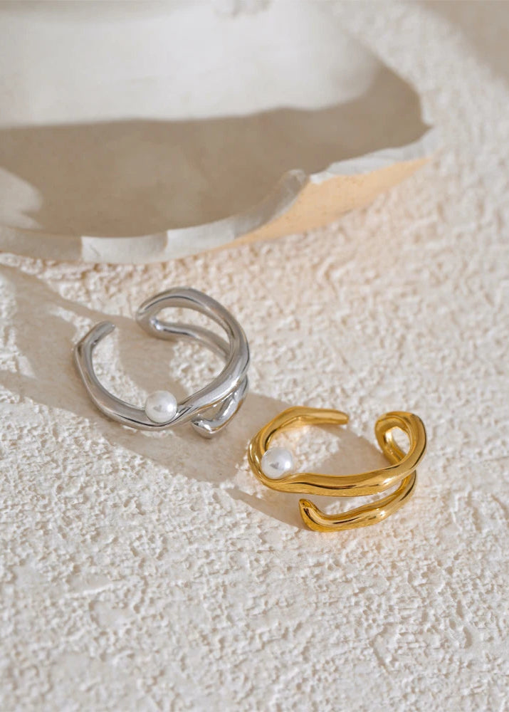 Two rings, one silver and one gold, on a textured white surface.