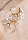 Pair of gold and pearl earrings on a beige surface