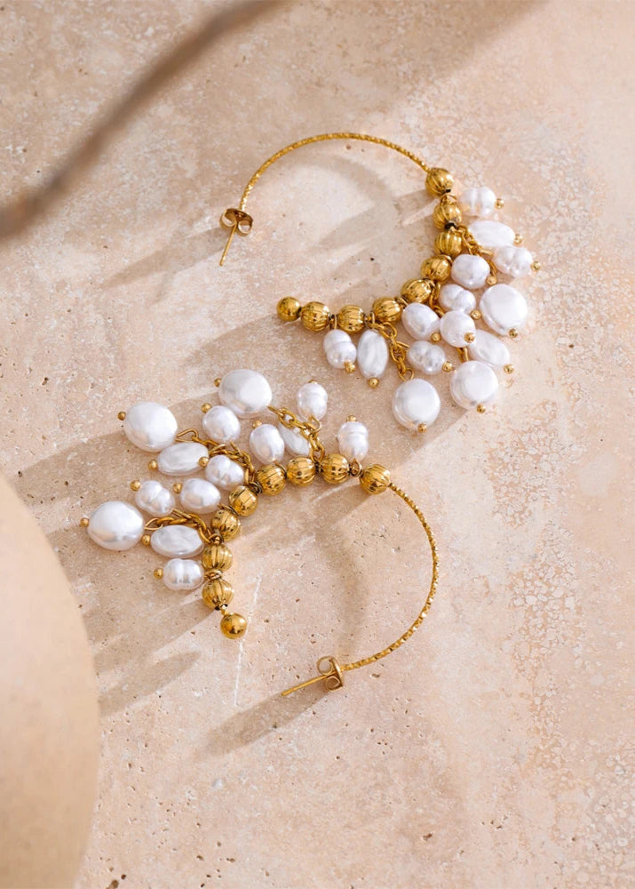 Pair of gold and pearl earrings on a beige surface