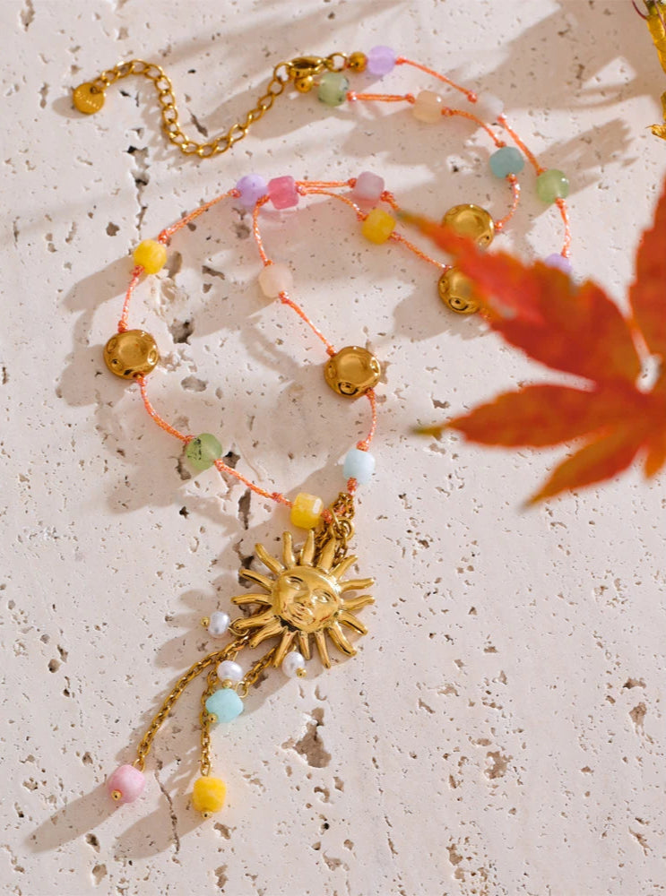 Colorful beaded necklace with a gold sun charm on a textured surface.
