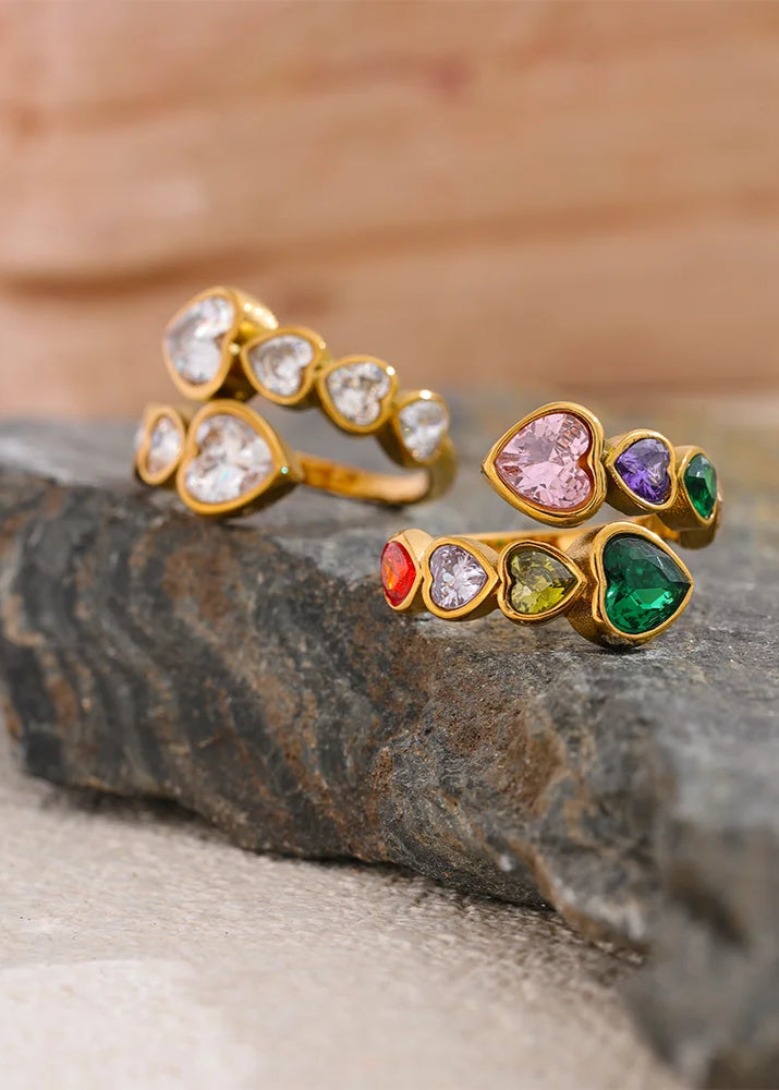 Two gold rings with colorful gemstones on a stone surface