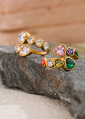 Two gold rings with colorful gemstones on a stone surface