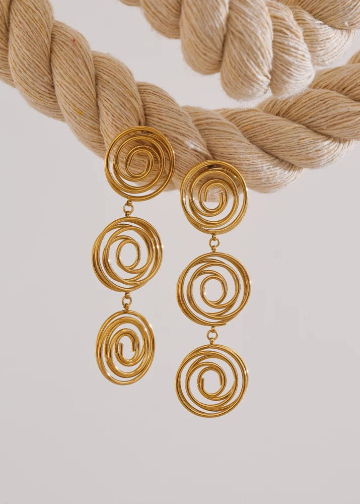 Gold spiral earrings with braided beige yarn on a light gray background