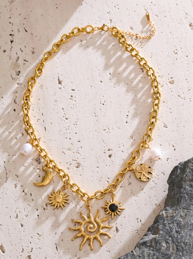 Gold necklace with sun and moon charms on a textured stone surface