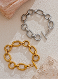 Two chain bracelets, one gold and one silver, on a textured surface.