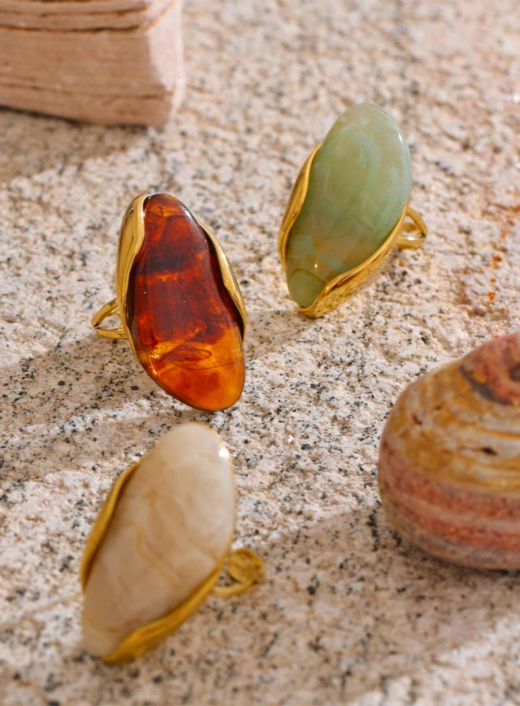 Three gemstone rings with gold settings on a textured surface