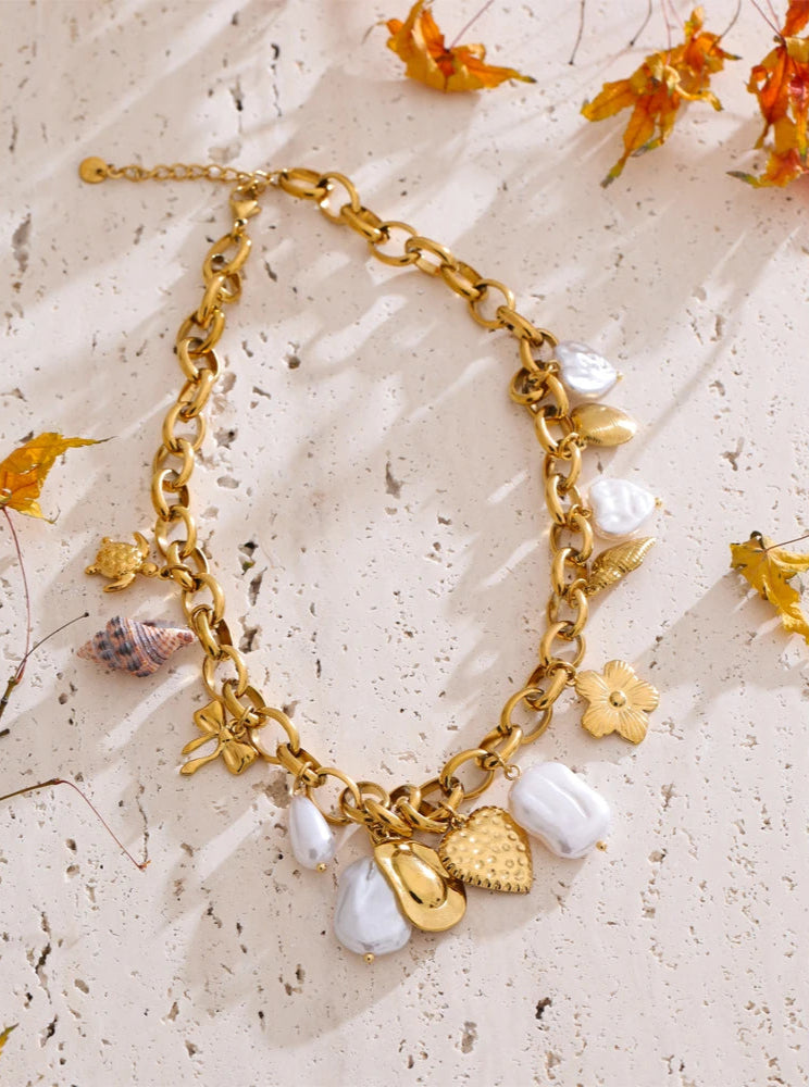 Gold bracelet with charms on a textured beige surface with dried flowers.