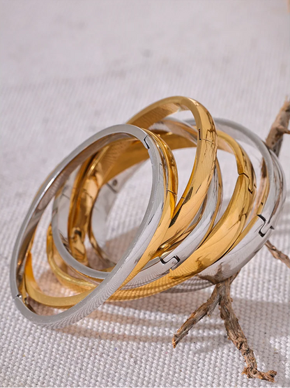 Stack of gold and silver bracelets on a textured surface with a branch.