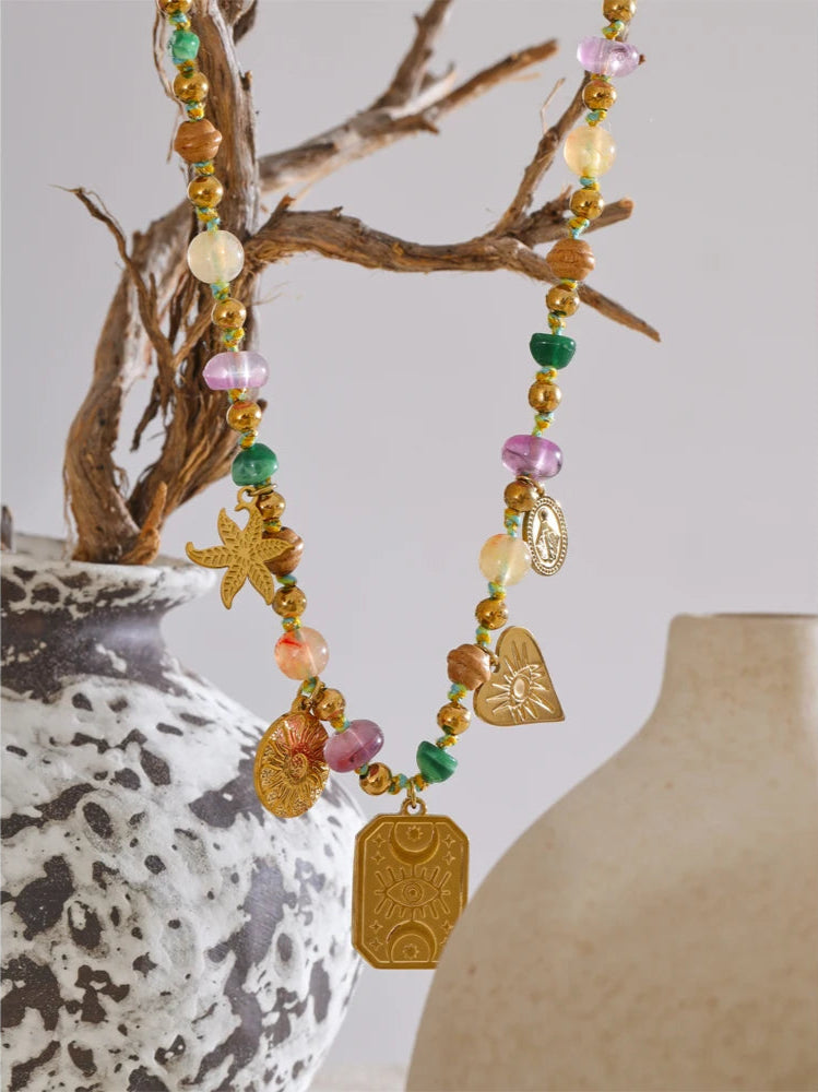 Colorful beaded necklace with starfish and heart charms hanging over a textured vase.