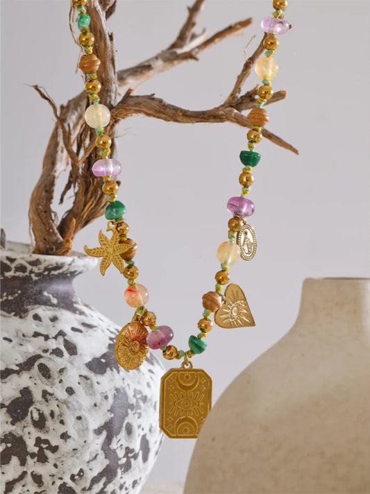 Colorful beaded necklace with starfish and heart charms hanging over a textured vase.