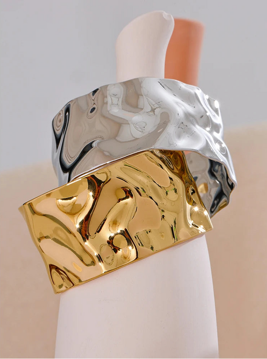 Gold and silver cuff bracelet on a mannequin arm against a neutral background