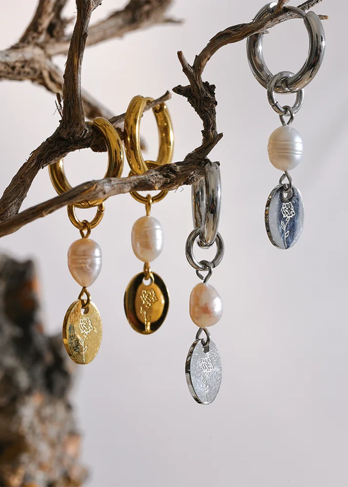 Three pairs of earrings with pearl and metallic charms hanging from a branch.