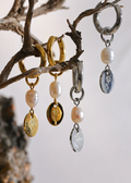 Three pairs of earrings with pearl and metallic charms hanging from a branch.
