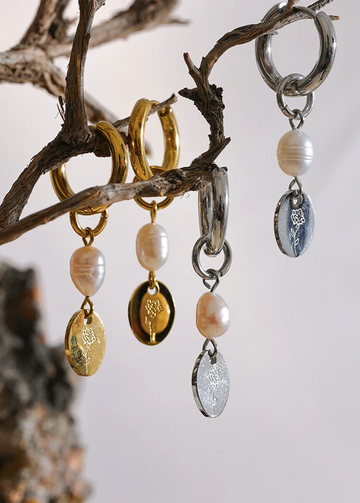 Three pairs of earrings with pearl and metallic charms hanging from a branch.