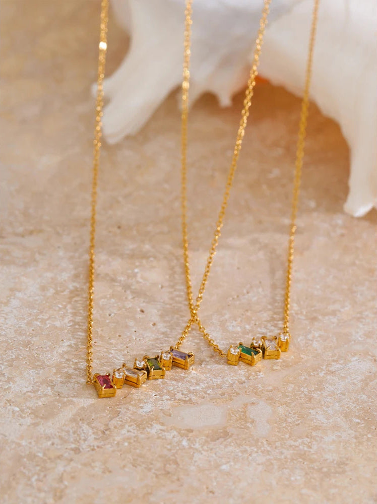 Gold necklaces with gemstones on a textured surface