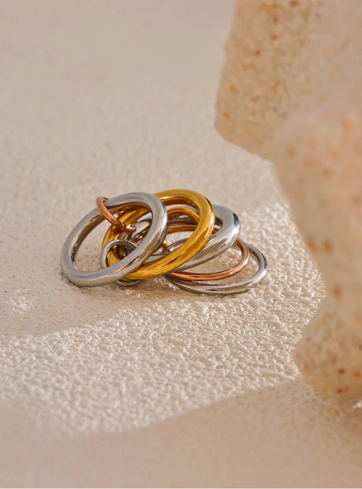 Three interlocking rings in silver, gold, and bronze on a textured beige surface.