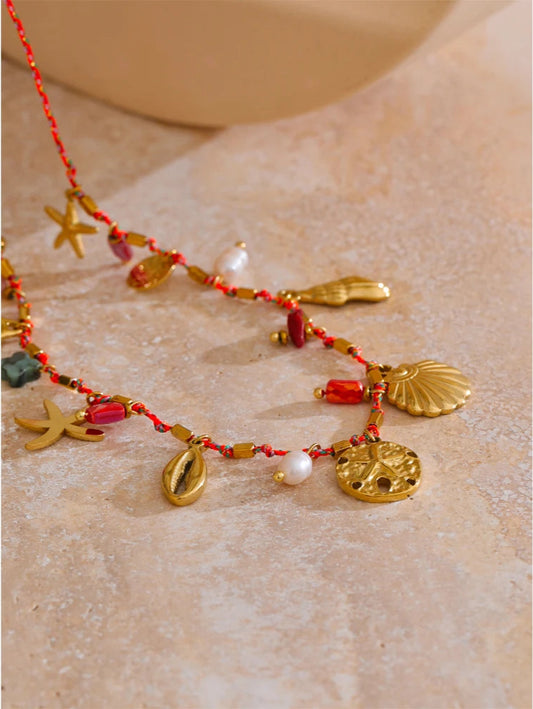 Beach themed Necklace with gold and red beads and charms on a textured beige surface