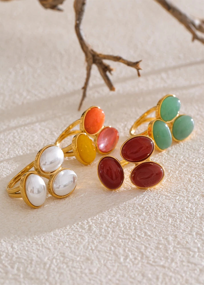 Set of colorful gemstone rings on a textured surface with a branch in the background