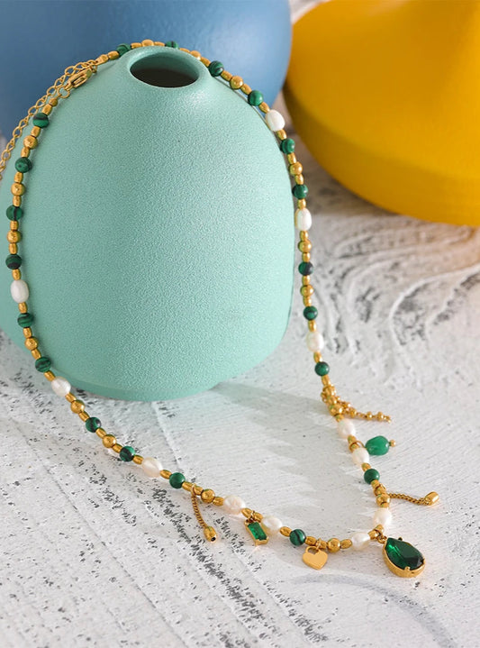 Vintage style Necklace with green and gold beads on a textured surface with colorful vases in the background