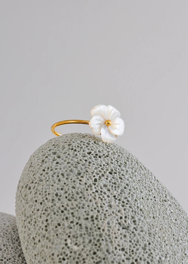Gold earring with a white flower on a textured gray surface