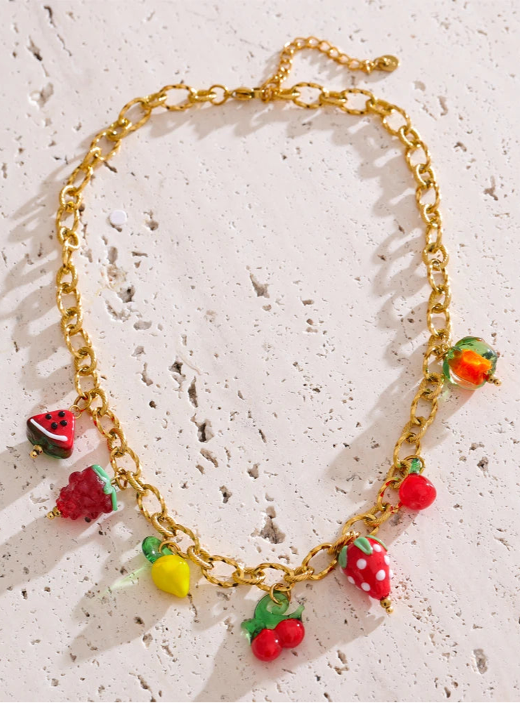 Gold chain necklace with colorful fruit-shaped charms on a textured white surface