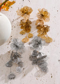 Pair of floral earrings in gold and silver on a textured white surface.