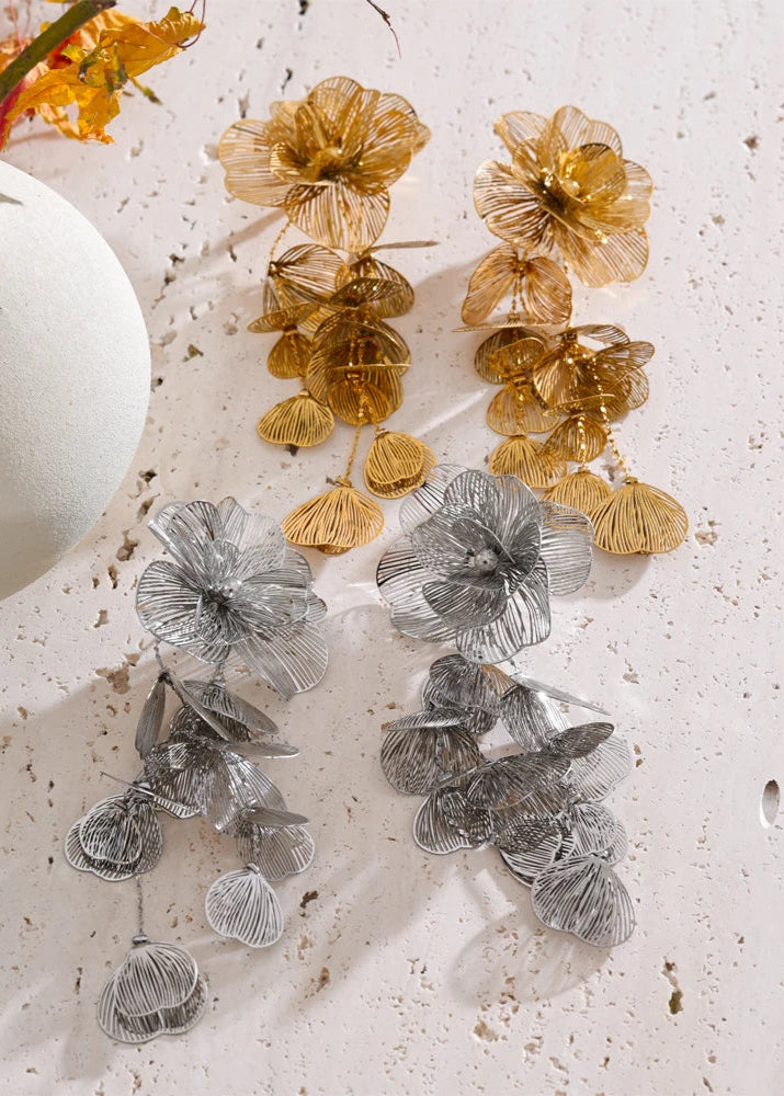 Pair of floral earrings in gold and silver on a textured white surface.