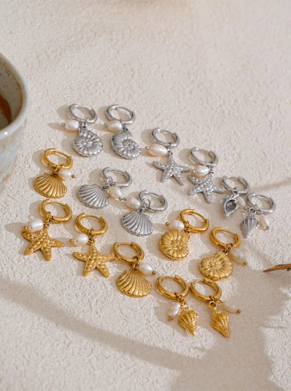 Collection of gold and silver seashell earrings on a textured surface with a cup in the corner.