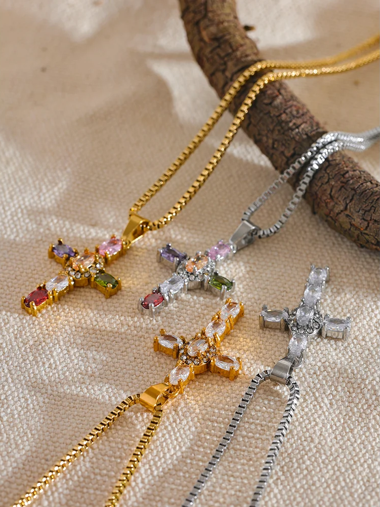 four golden and silver cross-shaped necklaces with gemstones on a textured surface
