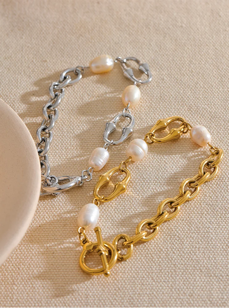 Two pearl-encrusted bracelets, one gold and one silver, on a beige surface.