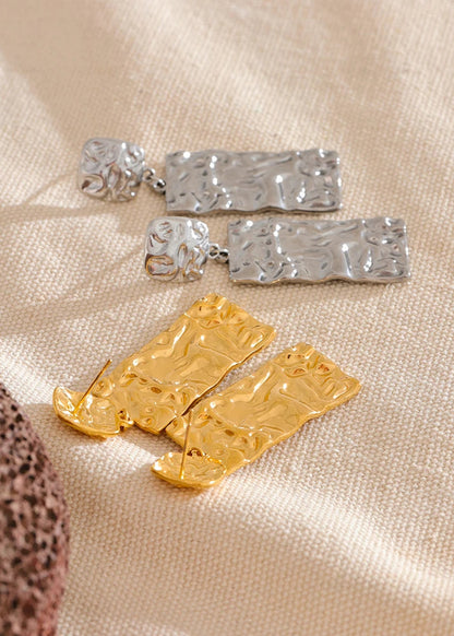 Gold and silver earrings on a textured beige surface