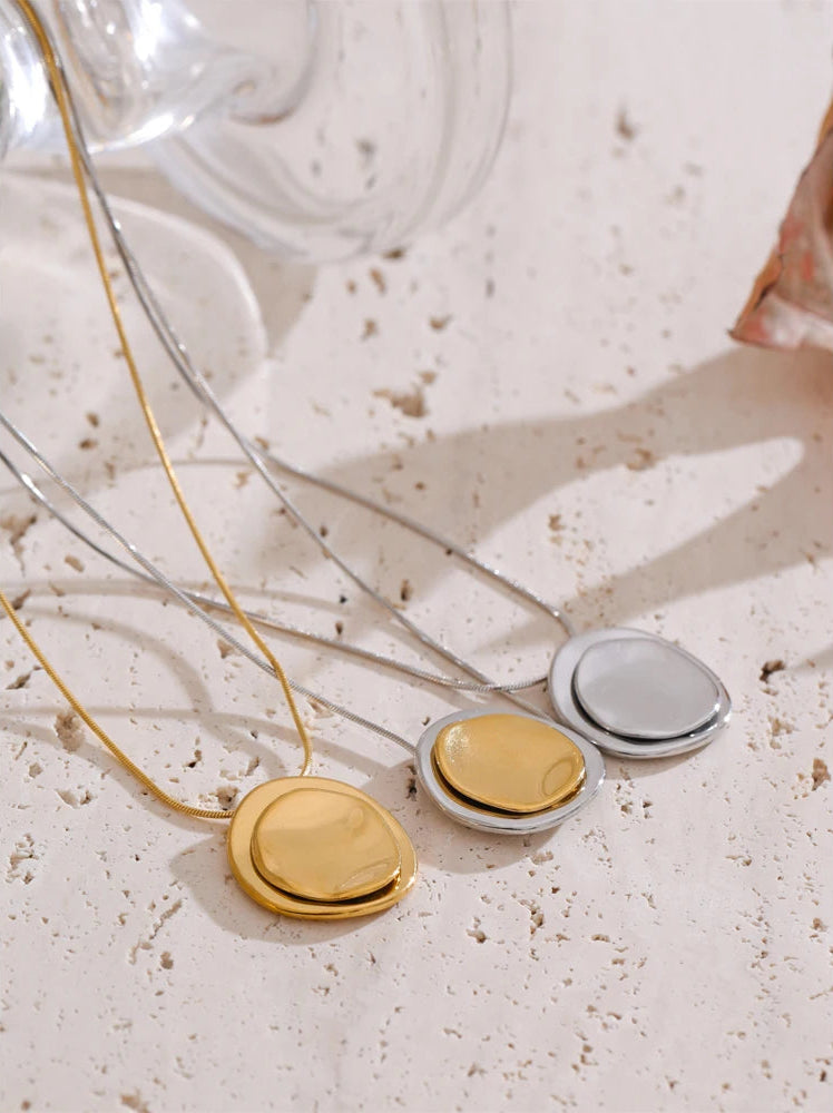 Three necklaces with round pendants in gold, silver, and bronze on a textured surface.