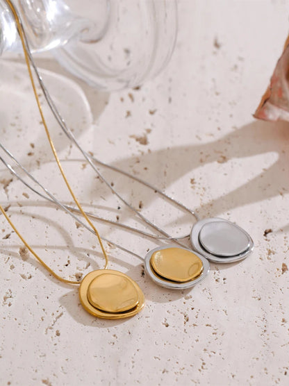 Three necklaces with round pendants in gold, silver, and bronze on a textured surface.