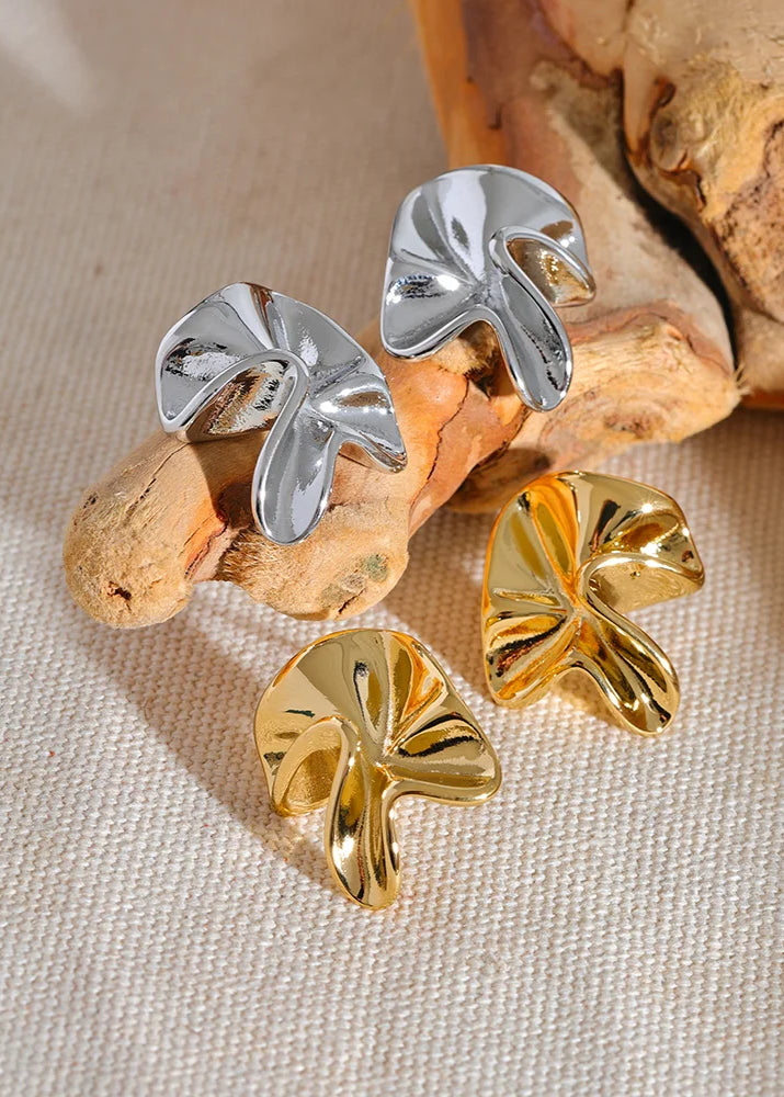 Pair of silver and gold leaf-shaped earrings on a natural wood background