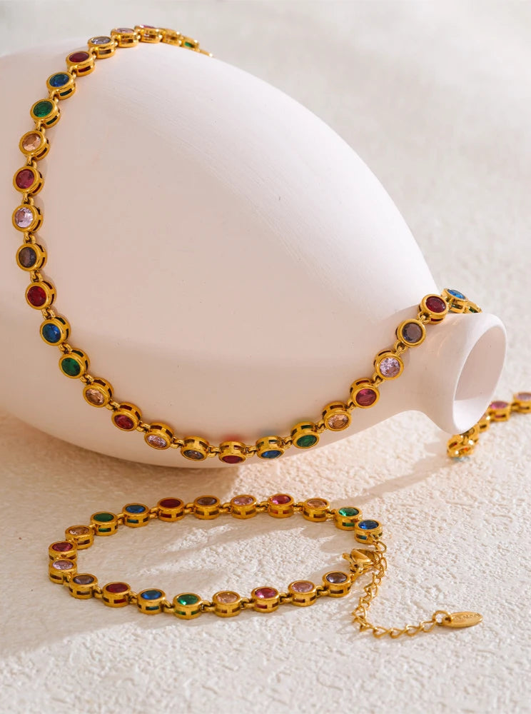 Gold bracelet and necklace with colorful gemstones on a white surface