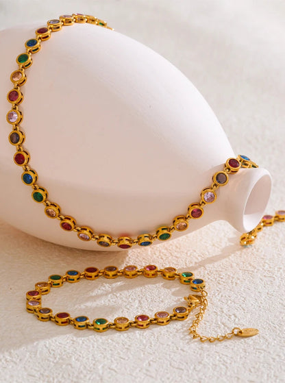 Gold bracelet and necklace with colorful gemstones on a white surface