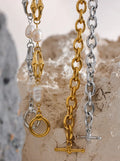 Three gold and silver chain necklaces on a textured stone surface.