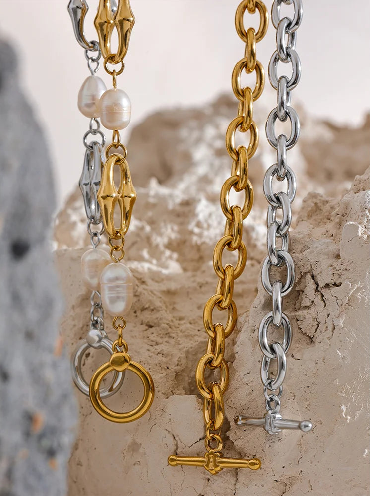 Three gold and silver chain necklaces on a textured stone surface.