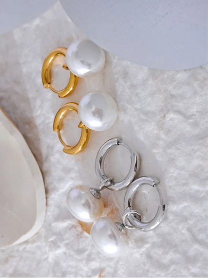 Pair of gold hoop earrings with pearls on a textured white surface