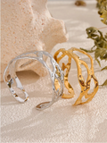 Gold and silver cuff bracelets on a textured surface with natural elements.